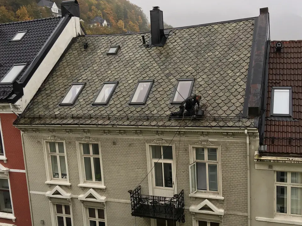Ouvrier encordé sur un toit en ardoise d'immeuble, nettoyant la gouttière.